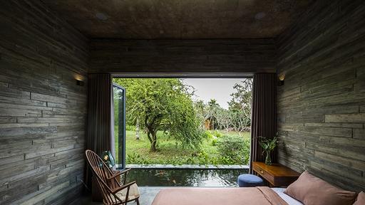 Thatched roof house sits next to a tranquil pond in Vietnam.