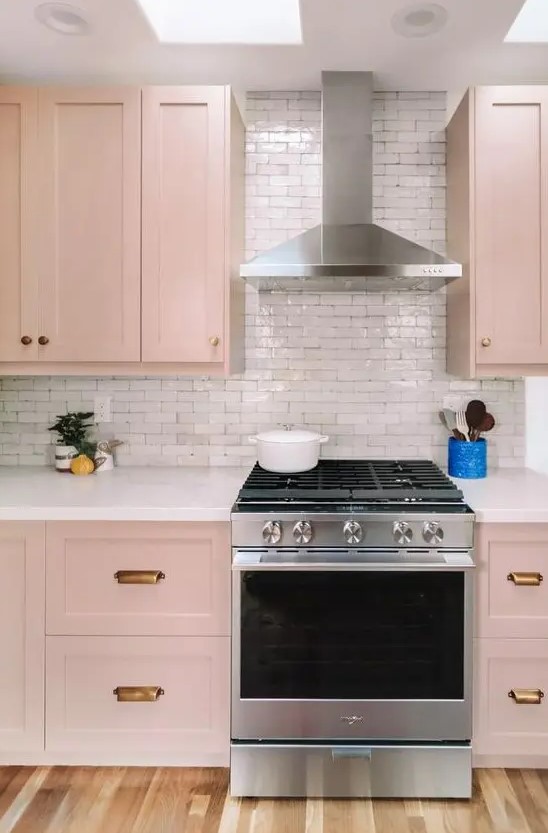 A beautiful blush kitchen with brass handles, a white tile backsplash and skylights is very delicate and delicate