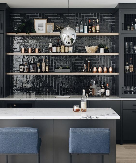 A black kitchen with a glossy black tile backsplash, open shelving, a gray island and navy stools is cool and chic