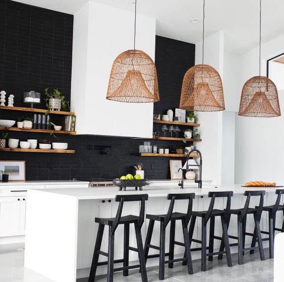 A black and white kitchen with sleek white cabinets, a white kitchen island, black stools, pendant lamps, a black tile backsplash and open shelving