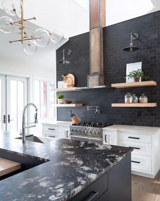 A black and white kitchen with white cabinets, a black tile backsplash, a black island and stone countertops