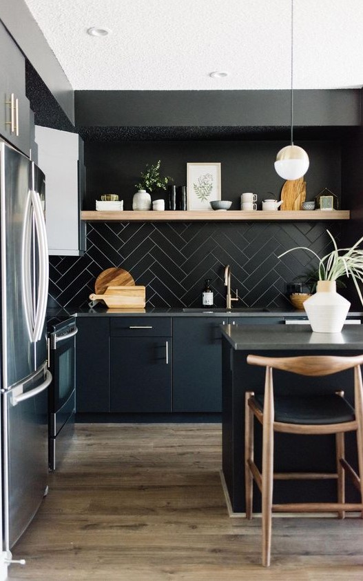 a chic black kitchen with black cabinets, a tiled backsplash, concrete countertops and light wood accents