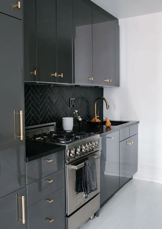 A glossy black kitchen with black chevron tiles on the backsplash and gold fixtures is a cool and chic idea in a classic color