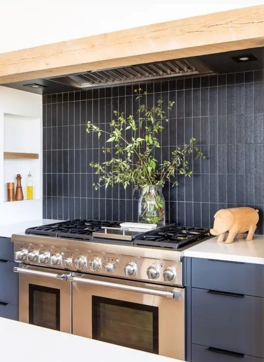 a gray kitchen with wooden beams, a black, matt, narrow tiled splashback and a metal stove and extractor hood