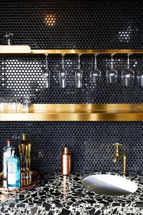 A black penny tile backsplash and gold shelves and fixtures create a very chic and sophisticated combination