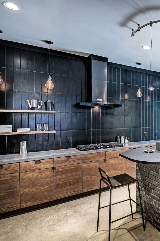 a minimalist stained kitchen with a gray quartz countertop and a black large stacked tile backsplash that takes up an entire wall
