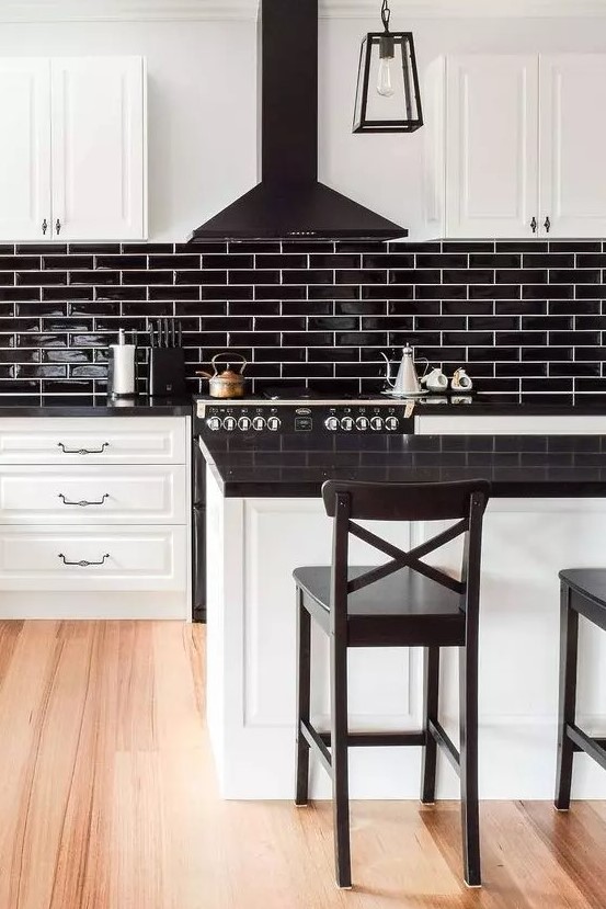 a modern farmhouse kitchen with white shaker cabinets and a kitchen island, black countertops, a black slim tile backsplash and a black range hood