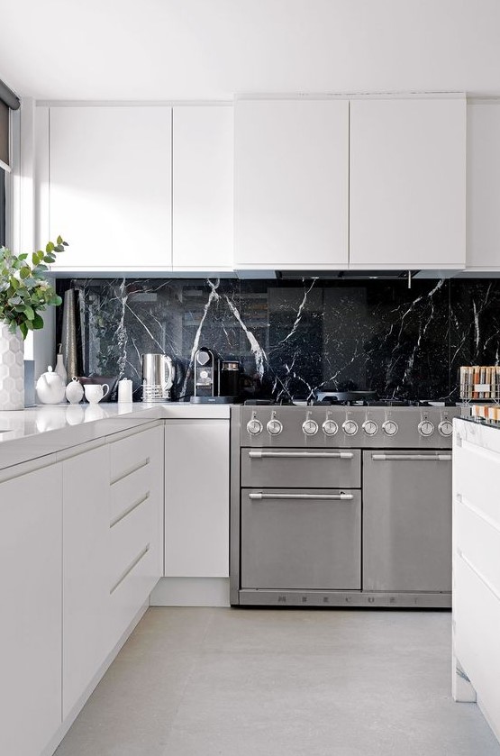 A black marble kitchen backsplash adds a very luxurious touch to these ultra-minimalist white cabinets