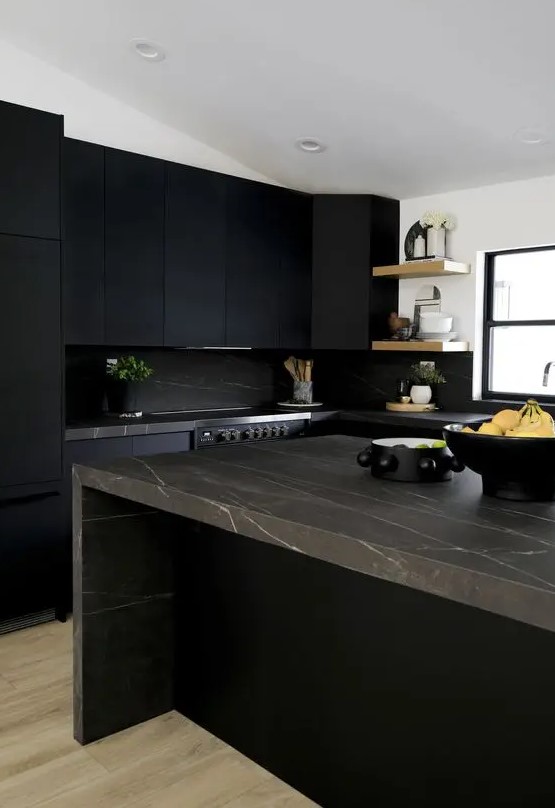 A matte black kitchen with a black marble backsplash and brown marble countertops, open shelving and some potted plants