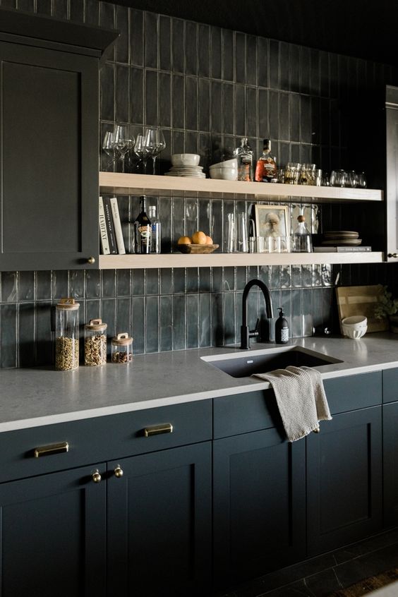 A moody farmhouse kitchen with navy blue cabinets, white countertops, a gray slim tile backsplash and open shelving