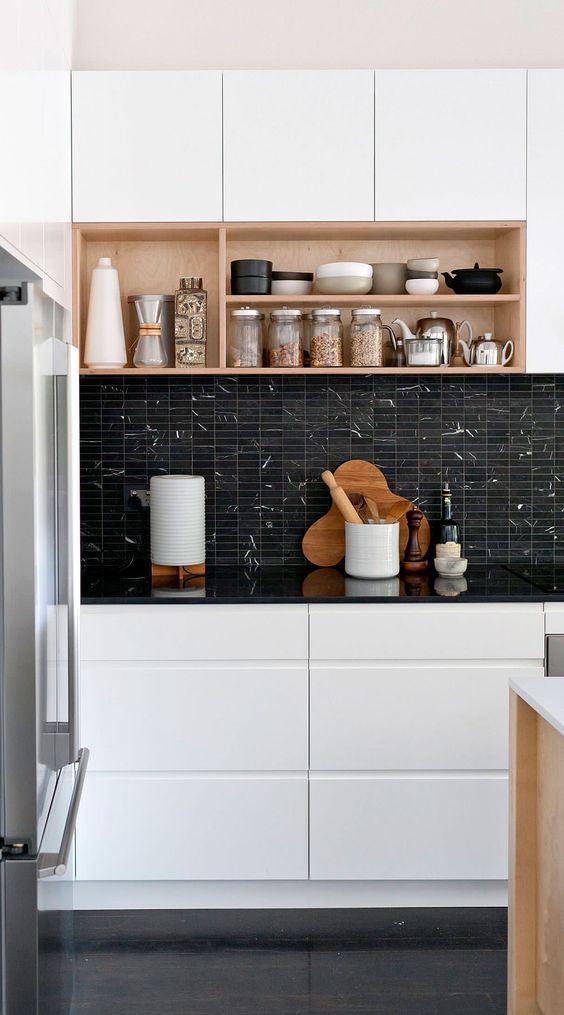 A stylish modern kitchen with sleek white cabinets, a black stacked tile backsplash and black countertops and box shelves