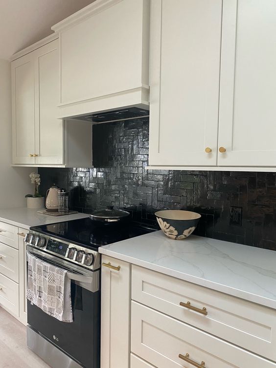 A white farmhouse kitchen with shaker-style cabinets, a black herringbone tile backsplash, and white stone countertops