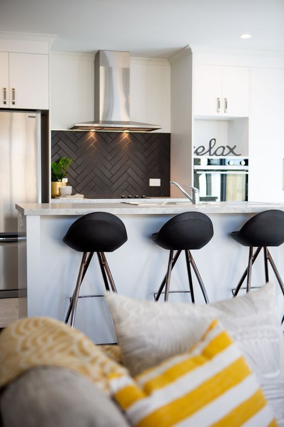 A small white kitchen with a black herringbone tile backsplash, black stools and some greenery is a cool solution
