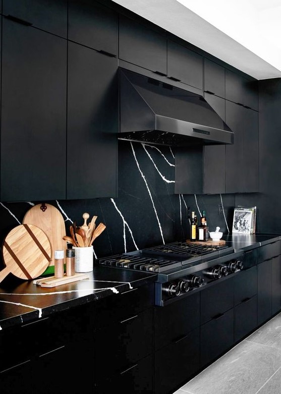a sophisticated black kitchen with metal cabinets, a marble backsplash and countertops, and a black extractor hood