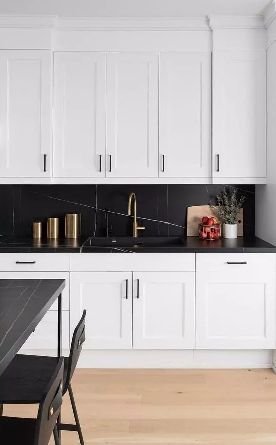 a sophisticated kitchen with white shaker cabinets, a chic black marble backsplash and countertop, a black table and chairs