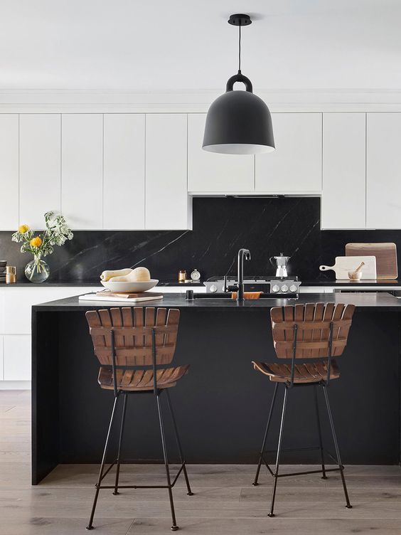 a beautiful white kitchen with elegant cabinets, a black marble backsplash and countertops, a black kitchen island, a black pendant lamp and wooden stools