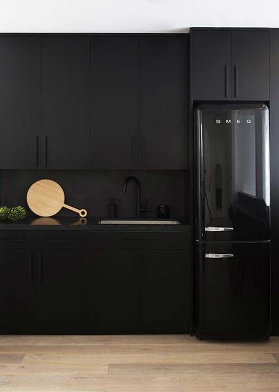 An all-black kitchen with matte cabinets, a matte backsplash, and a glossy refrigerator is a bold idea