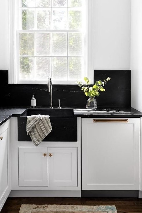 a white farmhouse kitchen with black quartz countertops and matching backsplash and mismatched metals for fixtures
