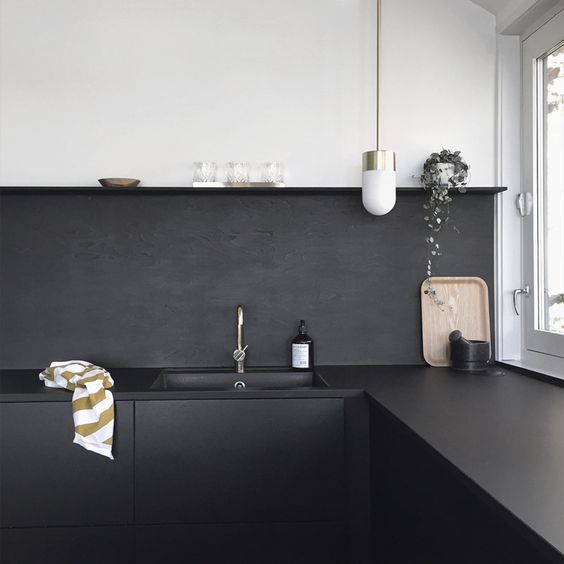 A matt black painted kitchen backsplash is a cost-effective idea and continues the decor of the kitchen with black cabinets and worktops