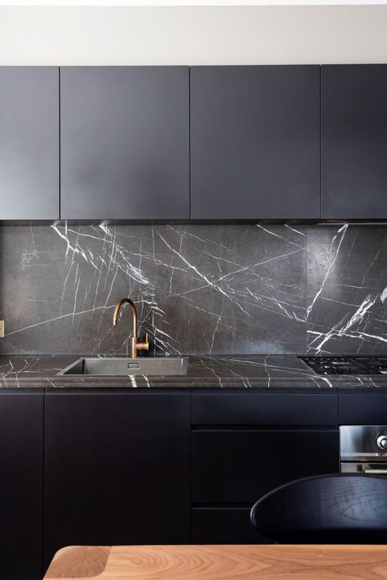 a minimalist midnight blue kitchen with elegant black marble cabinets, backsplashes and countertops and brass fittings