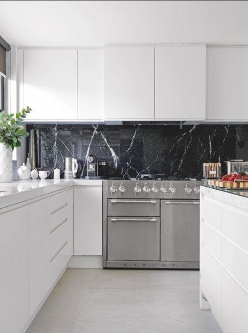 A pure white minimalist kitchen with a black marble backsplash that adds a sophisticated and chic touch