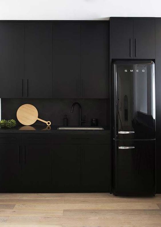 Matt black cabinets, a matt black back wall and a glossy black refrigerator for an unusual, atmospheric kitchen