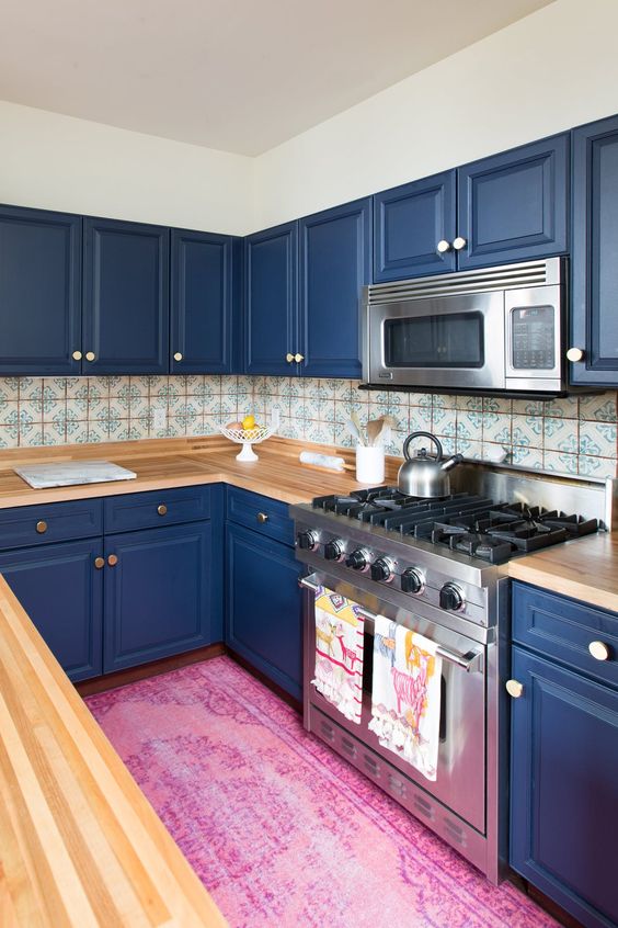 a bold blue kitchen with light wood countertops and a mosaic tile backsplash