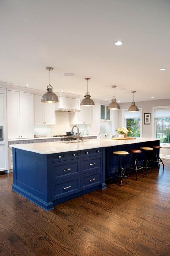 A white kitchen is enhanced by a large, bold blue island covered in white to connect with the space