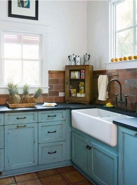 A blue shabby chic blue kitchen with dark countertops and a red faux brick backsplash for texture