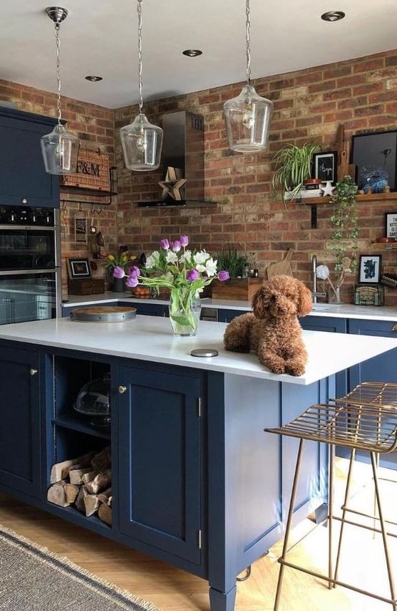 A bright blue kitchen with white countertops and glass pendant lamps is made more striking by red brick walls