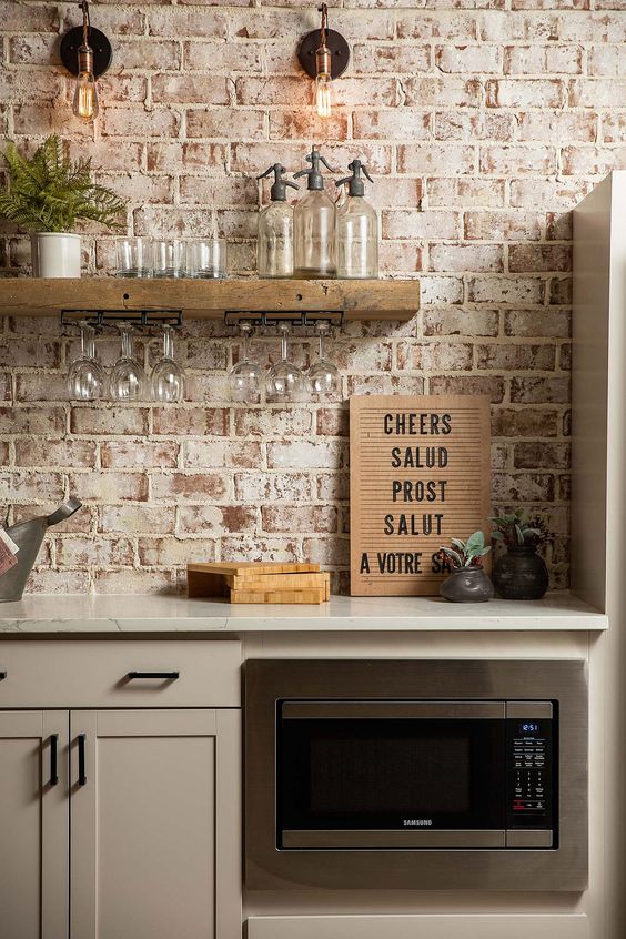 A dove gray kitchen with shaker cabinets, white stone countertops, open shelving and a whitewashed red brick backsplash