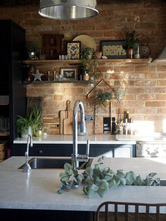 a navy blue kitchen with white stone countertops, open shelving, green plants and pendant lamps, and a red brick backsplash