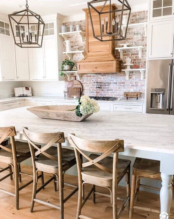 a neutral farmhouse kitchen with white cabinets, a red brick backsplash, and some metal lanterns over the island