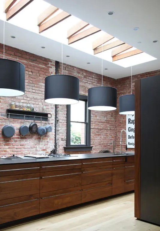 A red brick wall and richly stained wood cabinets create a masculine vibe in the kitchen, with black pendant lamps above