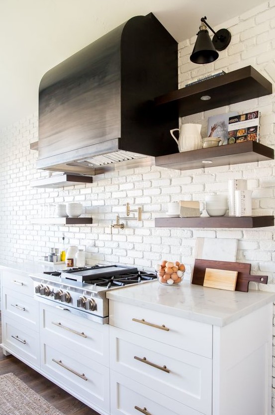 A vintage kitchen with white cabinets, copper hardware and a white faux brick wall highlighting the range hood