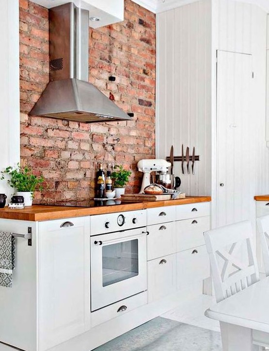 an inviting, modern farmhouse kitchen with white cabinets, richly stained countertops and a red brick wall