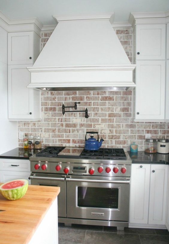 a white farmhouse kitchen with shaker-style cabinets, a whitewashed red brick backsplash, stainless steel appliances and black handles