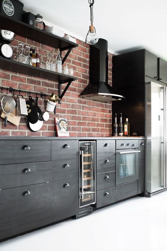 A stylish black kitchen with sleek cabinets, a red brick backsplash, and black appliances looks bold, contrasting, and super chic