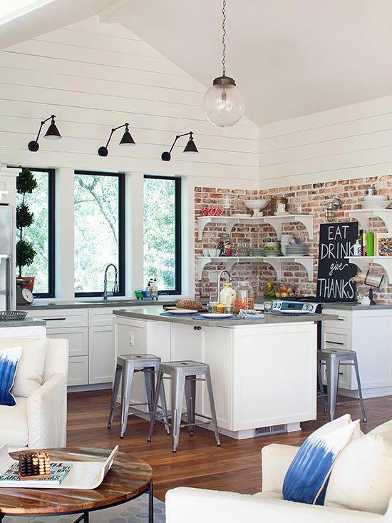 a modern white kitchen with white shaker style cabinets, gray stone countertops, open shelving and a red brick backsplash, black wall sconces and pendant lamps