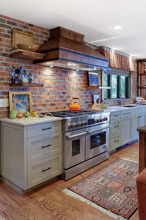 a gray kitchen with shaker-style cabinets, gray countertops, a red brick backsplash, a vintage metal hood, open shelving and lots of natural light