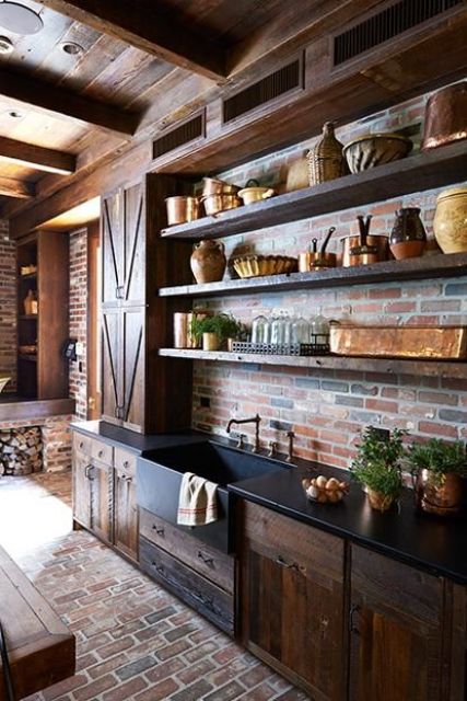 A rustic dark stained vintage kitchen with rough wood cabinets, black countertops, open shelving, a red brick backsplash and vintage appliances is amazing