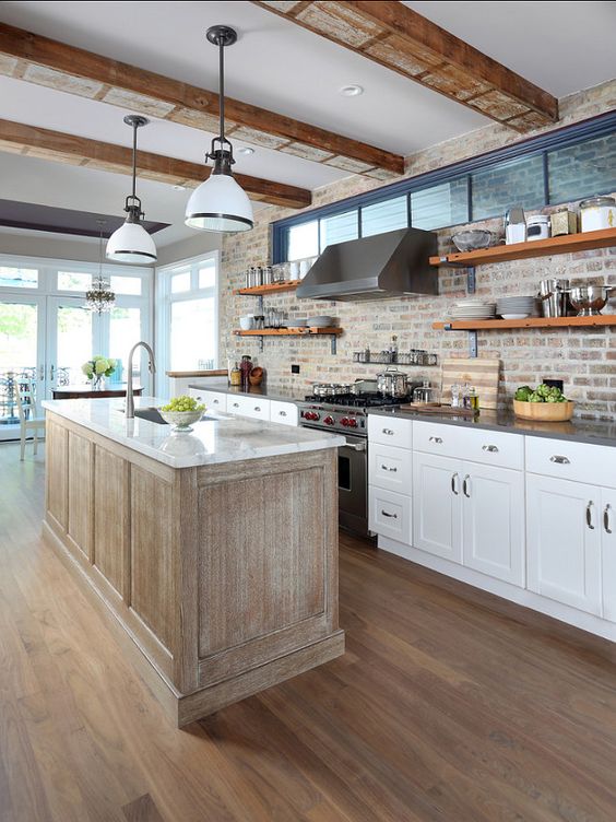 A pretty kitchen with white shaker-style cabinets, gray countertops, a brick backsplash, a rough wooden kitchen island and a white countertop is a chic and stylish idea