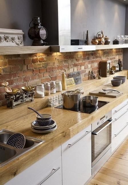 A beautiful Scandinavian kitchen with sleek white cabinets, wooden countertops, a red brick backsplash, built-in lights and open upper cabinets