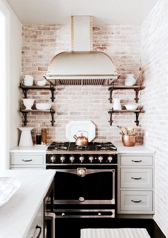 A vintage dove gray kitchen with shaker-style cabinets, a vintage stove, vintage range hood and open shelving, and a whitewashed brick backsplash