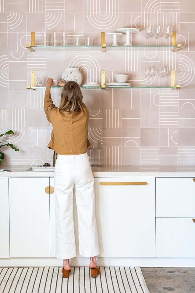 A delicate kitchen with elegant white cabinets, a pink geotile wall, glass and gold shelves is a very beautiful and unique idea