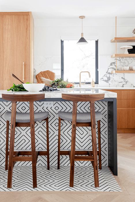 a light stained kitchen with white countertops and a marble backsplash, a chic kitchen island with black and white geotiles