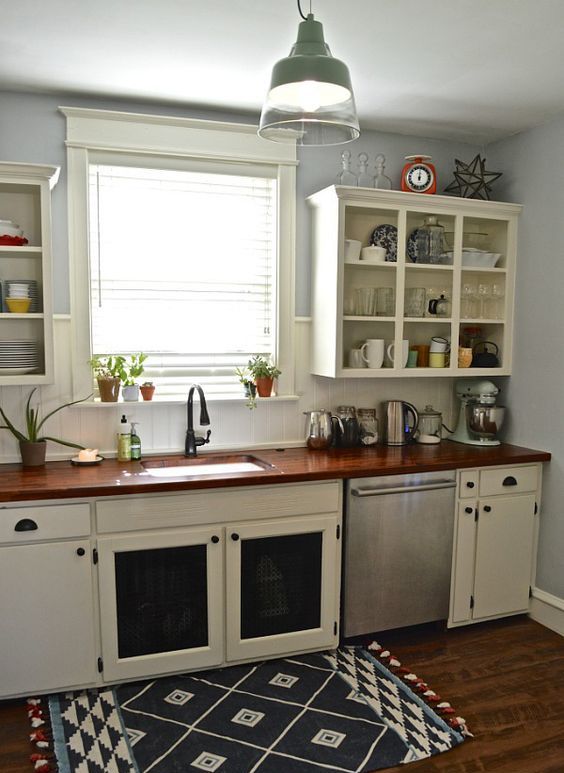 a simple, neutral kitchen with open upper cabinets, a dark-stained wood countertop and geoprint rug, and a green pendant lamp