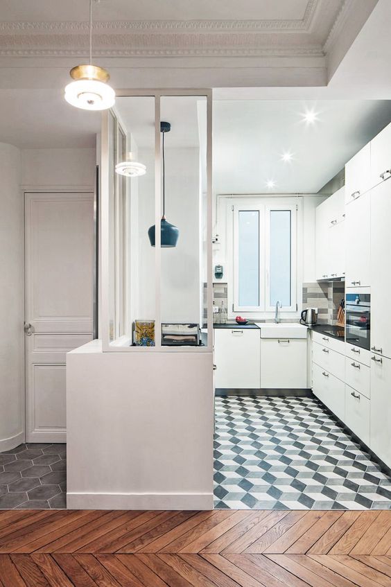 a modern white kitchen with black handles, a black and white geometric tile floor, a black pendant light and black countertops