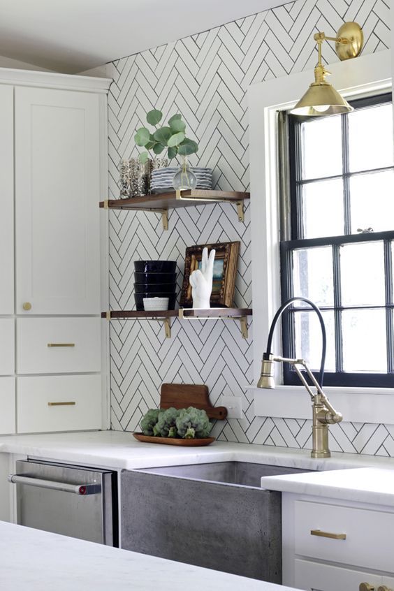 A white Scandinavian kitchen with a chevron tile wall, white stone countertops, and brass and gold accents is super chic