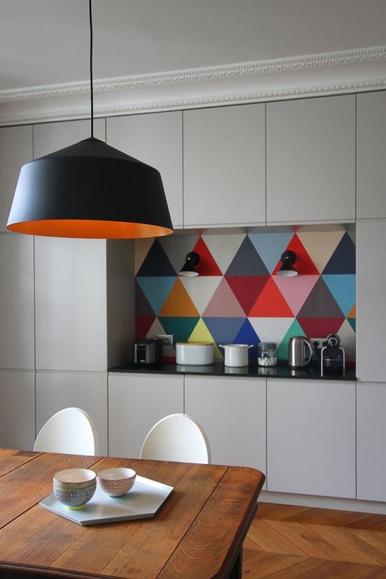 a neutral, modern kitchen with sleek cabinets, a colorful geotile backsplash, a black pendant lamp, and a wooden table